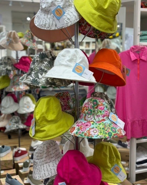 A display of various bucket hats in different colors and patterns, including floral designs and solid shades, arranged on a stand in a boutique. This women's boutique in Toronto features unique clothing and accessories. women’s boutique Toronto on Bayview