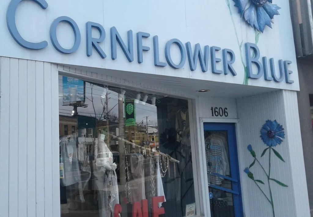 The storefront of a women's boutique named "Cornflower Blue" featuring a blue sign with large lettering and a flower illustration. The display includes clothing items and a "Sale" sign, located in Toronto, highlighting unique clothing options for local women’s fashion. women’s boutique Toronto on Bayview